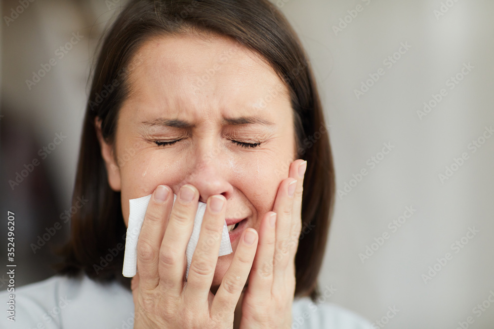 Close up portrait of frustrated adult woman crying hysterically with eyes closed and holding tissue, copy space Close up portrait of frustrated adult woman crying hysterically with eyes closed and holding tissue, copy space