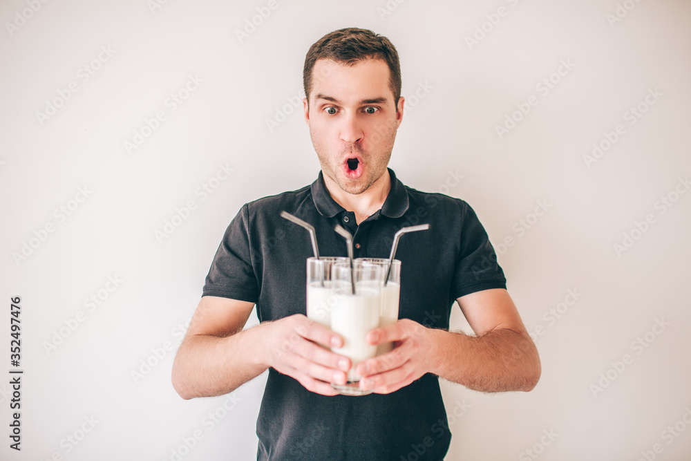 Young man isolated over white background. Amazed wondered guy hold three glasses with fresh milk or milkshake in hands. Black plastic straw inside. Young man isolated over white background. Amazed wondered guy hold three glasses with fresh milk or milkshake in hands. Black plastic straw inside.