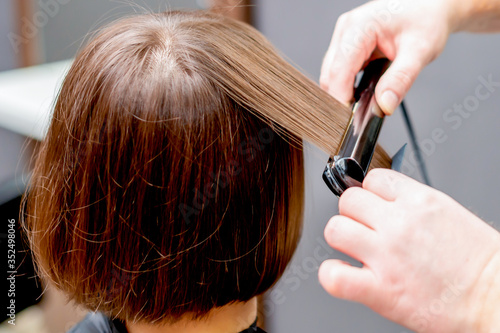 Hands of hairdresser straightening hair of woman in the hairdress studio.