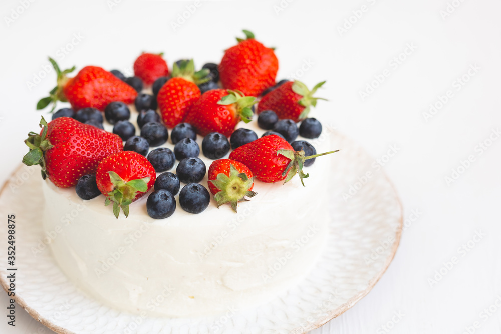 Close-up of white cream cake decorated with strawberries and blueberries on white handmade plate Close-up of white cream cake decorated with strawberries and blueberries on white handmade plate