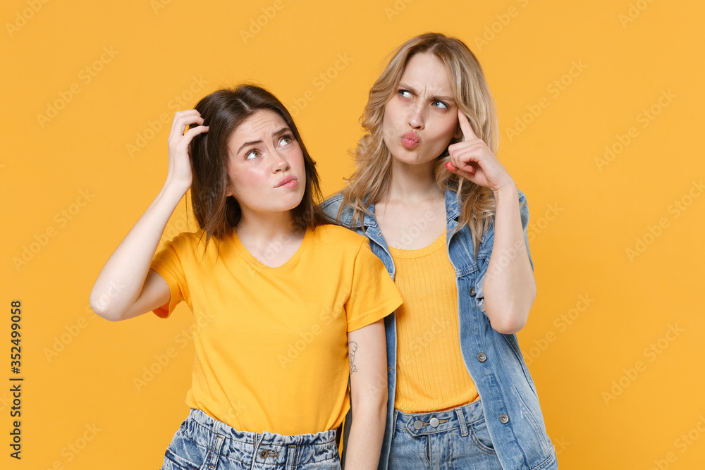 Two pensive puzzled young women girls friends in casual t-shirts denim clothes posing isolated on yellow background studio portrait. People lifestyle concept. Mock up copy space. Put hands on head. Two pensive puzzled young women girls friends in casual t-shirts denim clothes posing isolated on yellow background studio portrait. People lifestyle concept. Mock up copy space. Put hands on head.