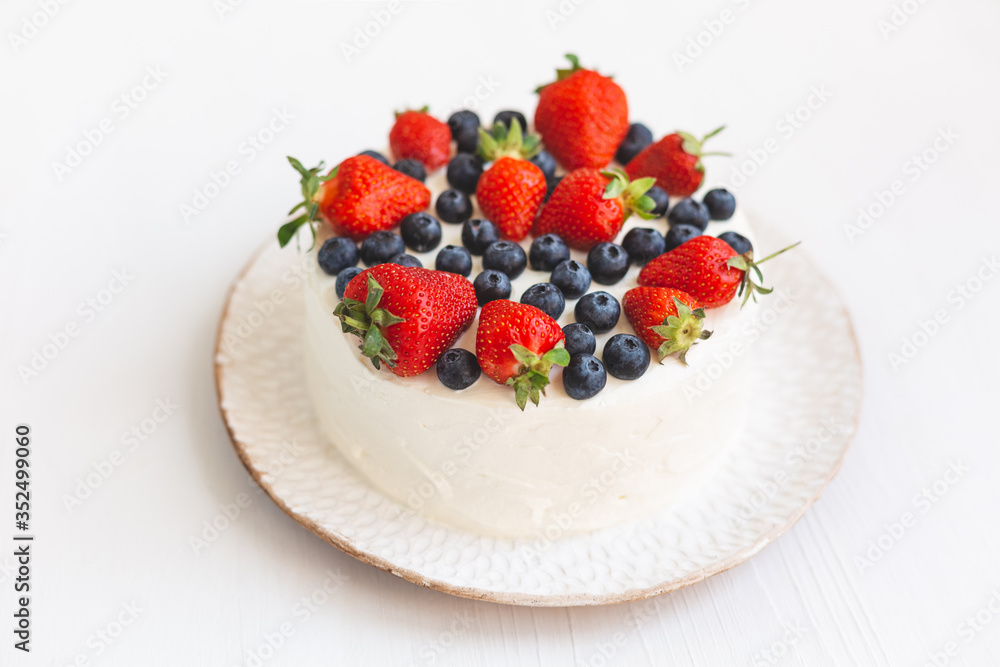 A beautiful appetizing cake with white cream and fresh summer berries decoration on hand made plate on white background. Delicious home made dessert with blueberries and strawberries A beautiful appetizing cake with white cream and fresh summer berries decoration on hand made plate on white background. Delicious home made dessert with blueberries and strawberries