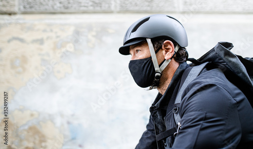 Delivery man courier with face mask and bicycle cycling in town.