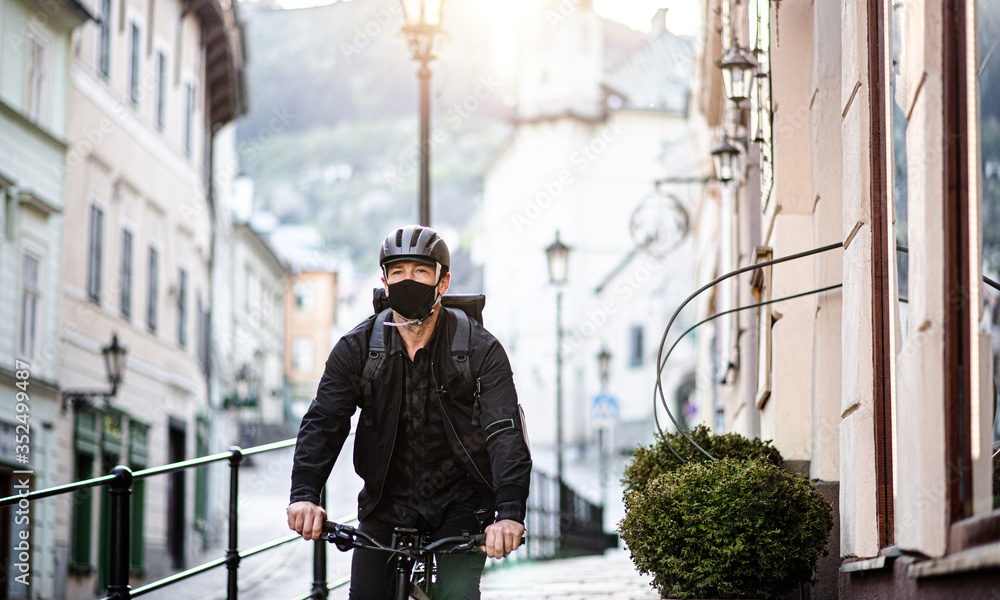 Delivery man courier with face mask and bicycle cycling in town.