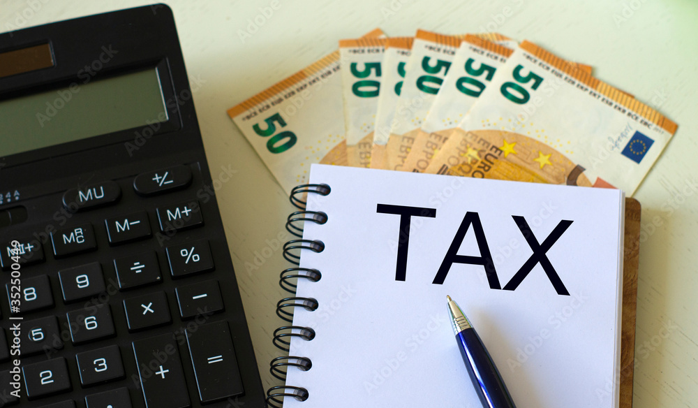TAX word in a notebook against the background of calculitar and banknotes TAX word in a notebook against the background of calculitar and banknotes