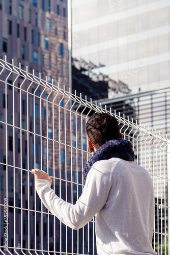 Young man leaning on a metallic fence while looking away to the business buildings