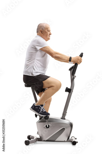 Full length profile shot of an elderly active man exercising on a stationary bike