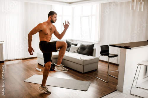 Young man doing exercising at home on the couch. Hardwoking t-shirtless guy sportsman in workout activity at his apartment. Trying to get better