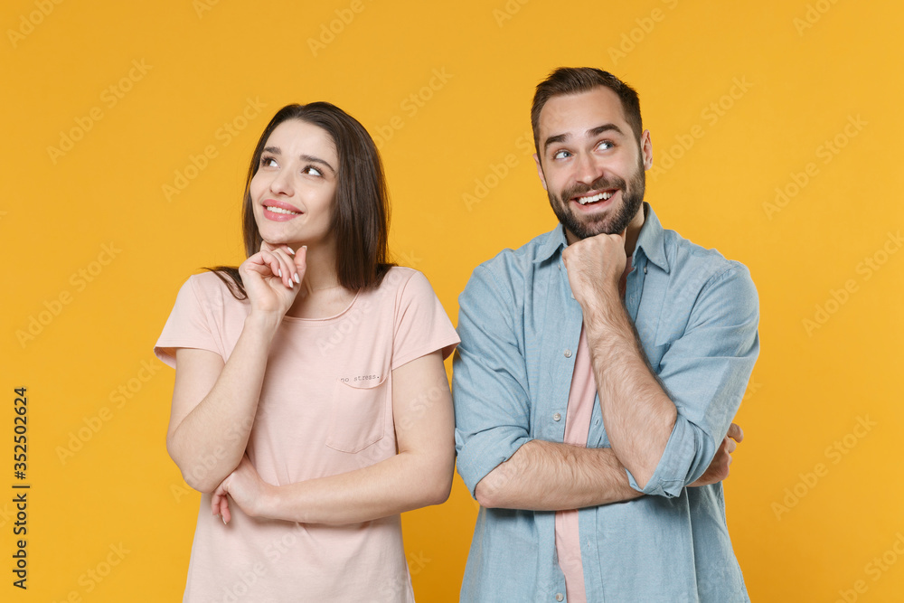 Pensive smiling young couple two friends guy girl in pastel blue casual clothes posing isolated on yellow background. People lifestyle concept. Mock up copy space. Put hand prop up on chin looking up. Pensive smiling young couple two friends guy girl in pastel blue casual clothes posing isolated on yellow background. People lifestyle concept. Mock up copy space. Put hand prop up on chin looking up.