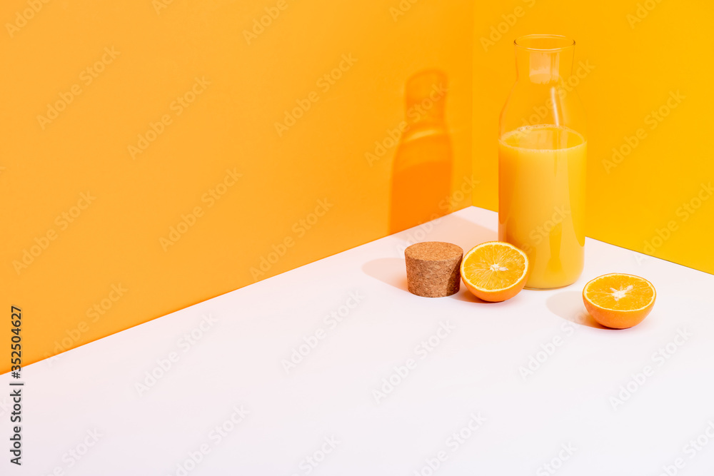 fresh orange juice in glass bottle near ripe oranges and cork on white surface on orange background fresh orange juice in glass bottle near ripe oranges and cork on white surface on orange background