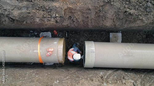 Concrete pipe tube installation. Aerial above men at work outside with heavy machinery to connect and install water or sewerage pipeline in a digging soil land