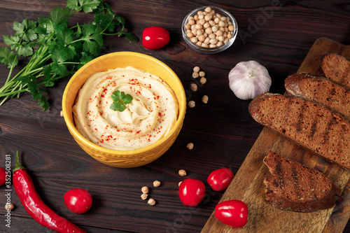 Plate of traditional hummus with crispy bread on wooden background