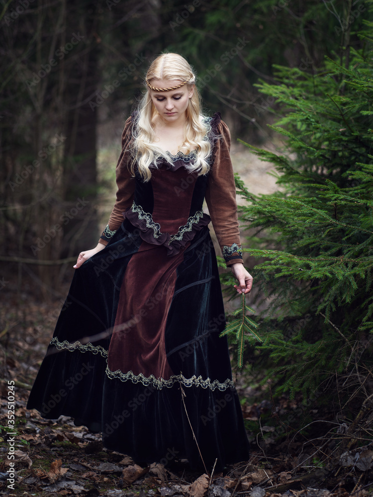 Beautiful girl dressed in stylish medieval clothes is training a beautiful horse in the forest. Fashion and style concept.