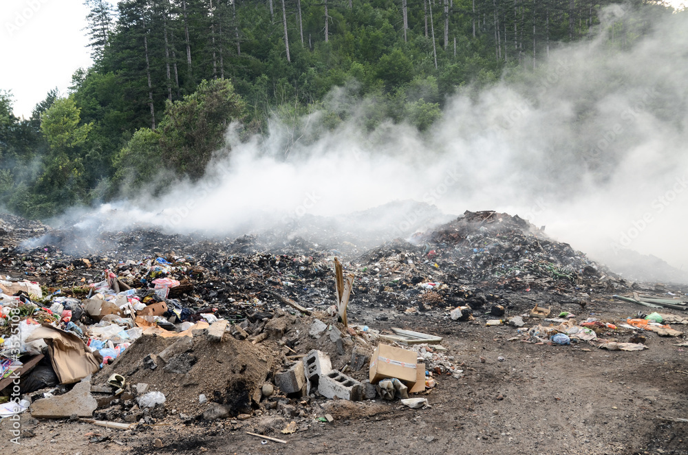 Open landfill site with burning waste. Burning pile of illegal garbage