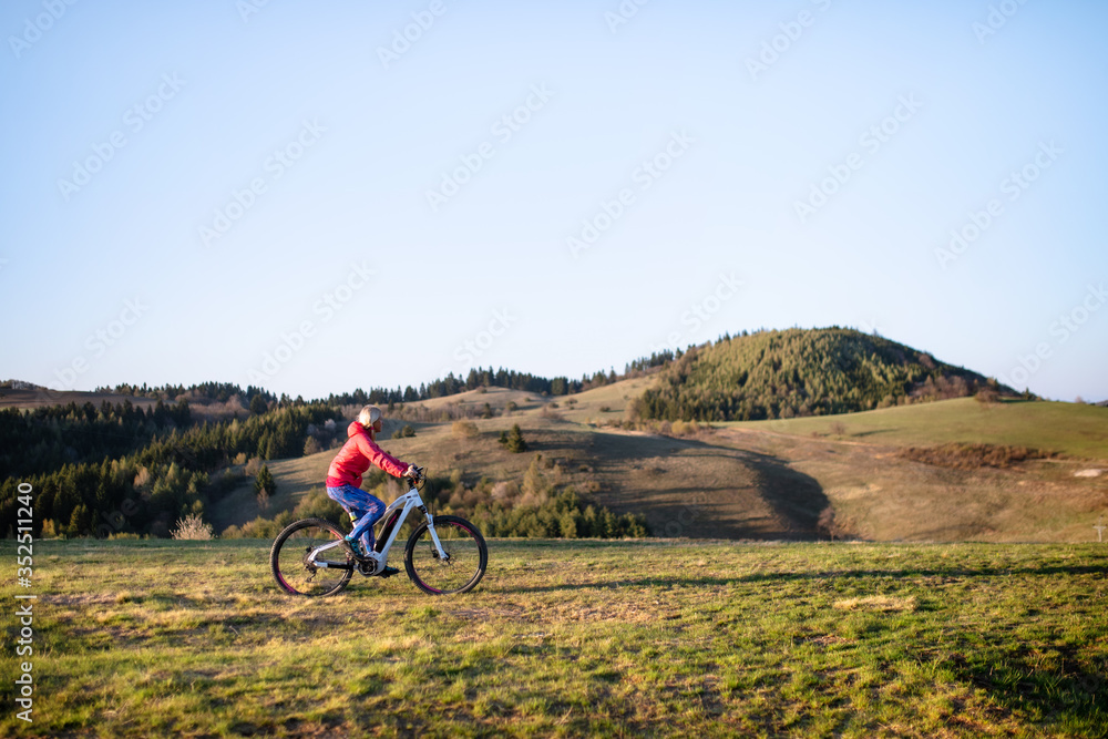 Active senior woman with e-bike cycling outdoors in nature.