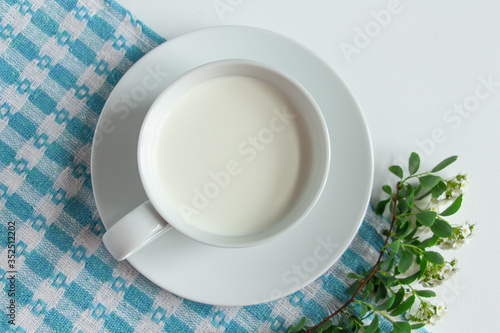 a white cup of fresh milk on a white background with sprigs of white flowers that complement the composition  tasty  healthy  atmospheric