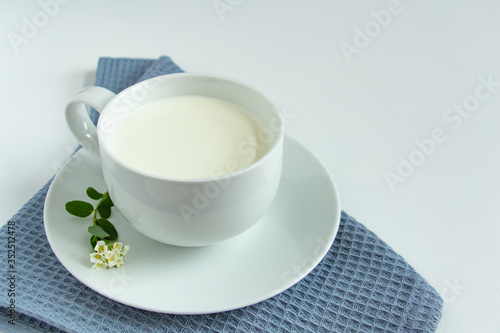 a white cup of fresh milk on a white background with sprigs of white flowers that complement the composition  tasty  healthy  atmospheric