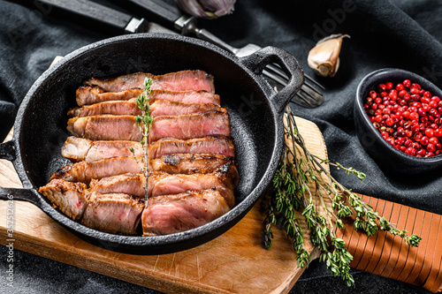 Fried sliced marble pork steak in a pan. Organic meat. Black background. Top view