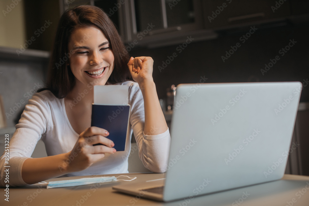 selective focus of cheerful freelancer holding passport with air ticket near laptop and medical mask, end of quarantine concept selective focus of cheerful freelancer holding passport with air ticket near laptop and medical mask, end of quarantine concept