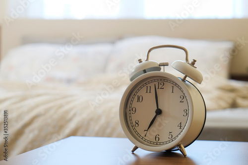 Rise and shine concept. Close up shot of white alarm clock showing 7 A.M. Unmade bed with morning light. Close up, copy space, background.