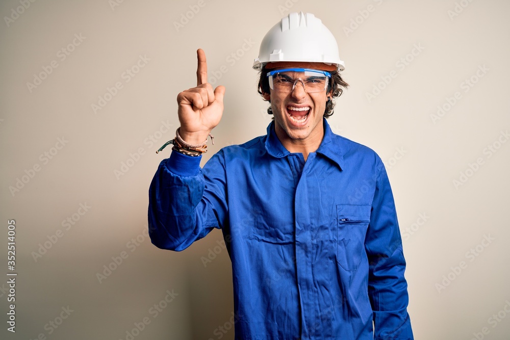 Young constructor man wearing uniform and security helmet over isolated white background pointing finger up with successful idea. Exited and happy. Number one.