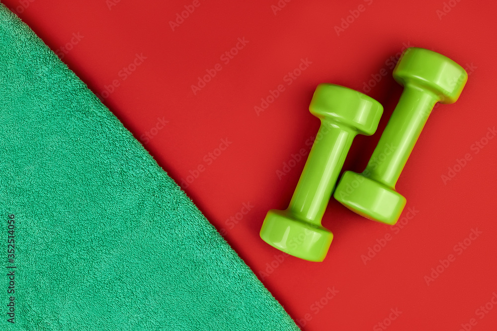 green dumbbells and towel on a red background. Layout, training plan for the season. Healthy lifestyle, concept for slimming body. It takes care of the body. green dumbbells and towel on a red background. Layout, training plan for the season. Healthy lifestyle, concept for slimming body. It takes care of the body.
