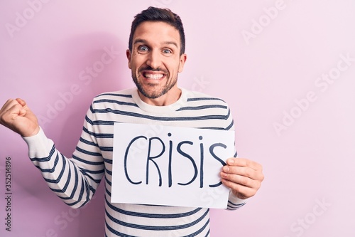 Young handsome man asking for economy holding paper with crisis word message screaming proud, celebrating victory and success very excited with raised arm © Krakenimages.com