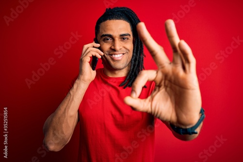 Young african american afro man with dreadlocks having conversation talking on smartphone doing ok sign with fingers, excellent symbol photo