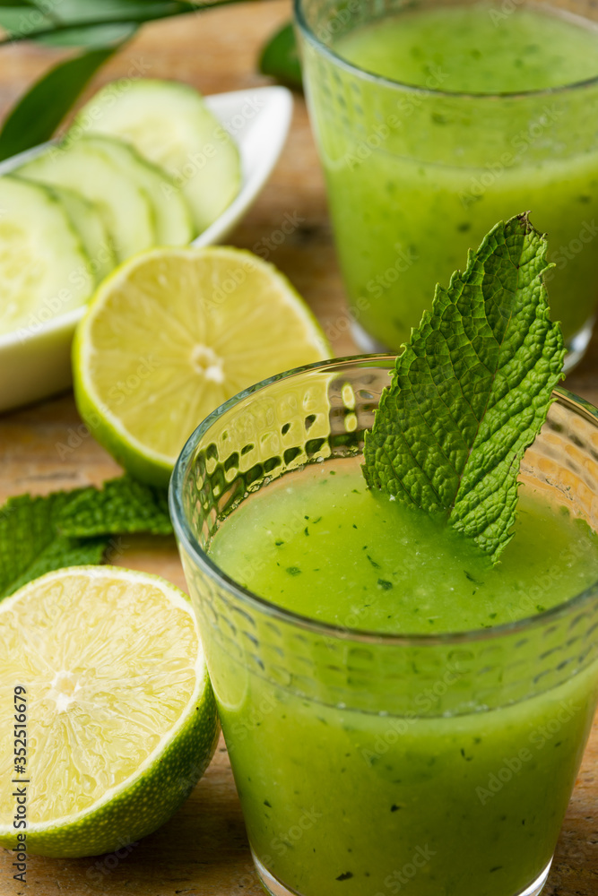 Aerial view of two glasses with cucumber juice, limes and mint, with selective focus, on wooden table, vertical Aerial view of two glasses with cucumber juice, limes and mint, with selective focus, on wooden table, vertical