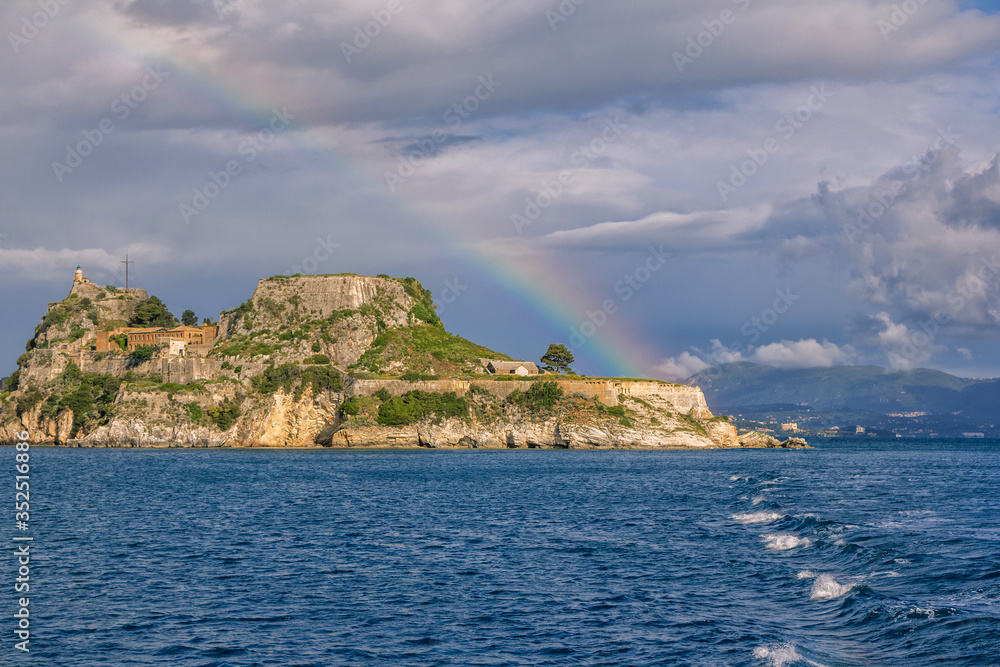 View of ancient venetian fortress on the hill at Corfu Island, Greece. Old stone walls, covered with green grass, sea bay, blue sky and rainbow