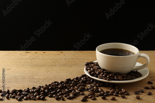 White coffee cup and coffee beans on wooden table with copyspace for text. Selective focus.