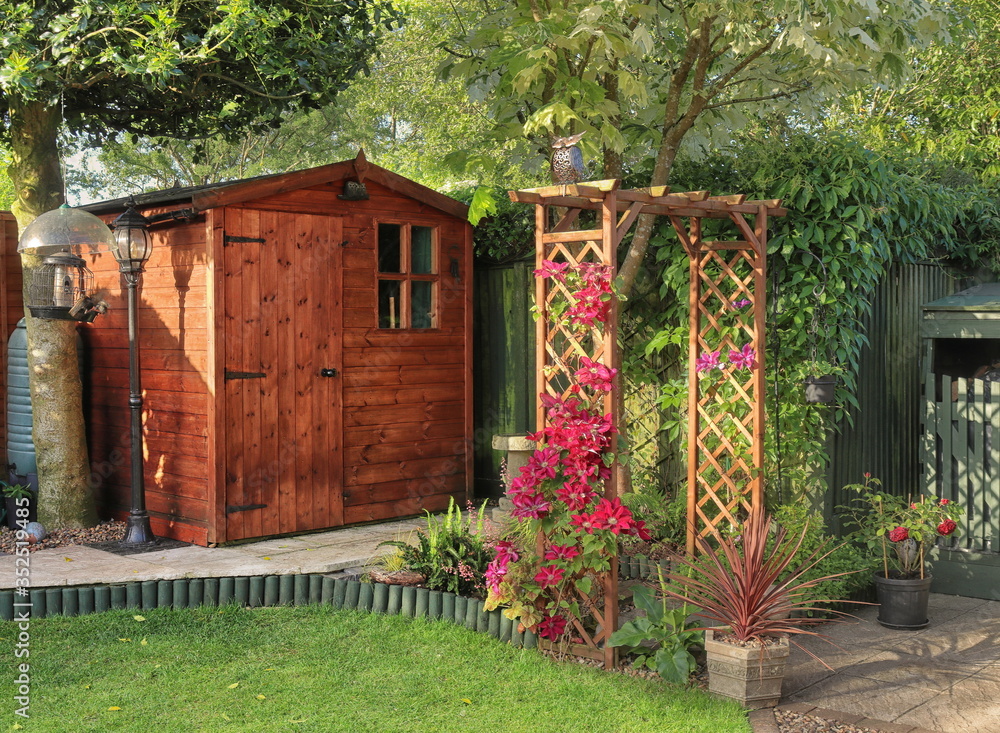 English back garden arch, gardening, clematis, flowers, blooms, horticulture, England, shed, building, cabin, storage, hedgerow, hedge, fence, patio, paving, foliage, plants, trees,