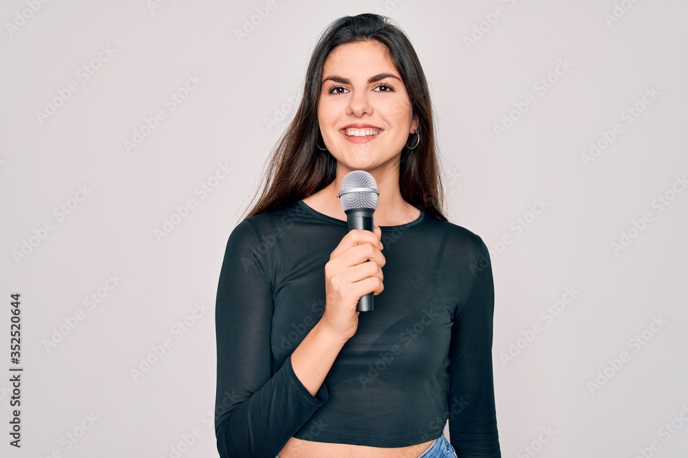 Young beautiful singer performer girl singing using music microphone over isolated background with a happy face standing and smiling with a confident smile showing teeth Young beautiful singer performer girl singing using music microphone over isolated background with a happy face standing and smiling with a confident smile showing teeth