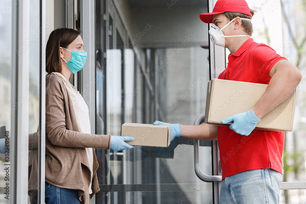 Courier in medical mask and gloves gives box to client, on porch Courier in medical mask and gloves gives box to client, on porch