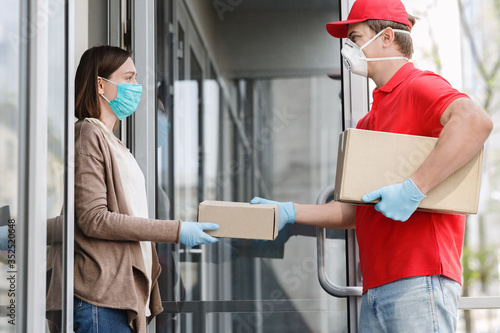 Courier in medical mask and gloves gives box to client, on porch