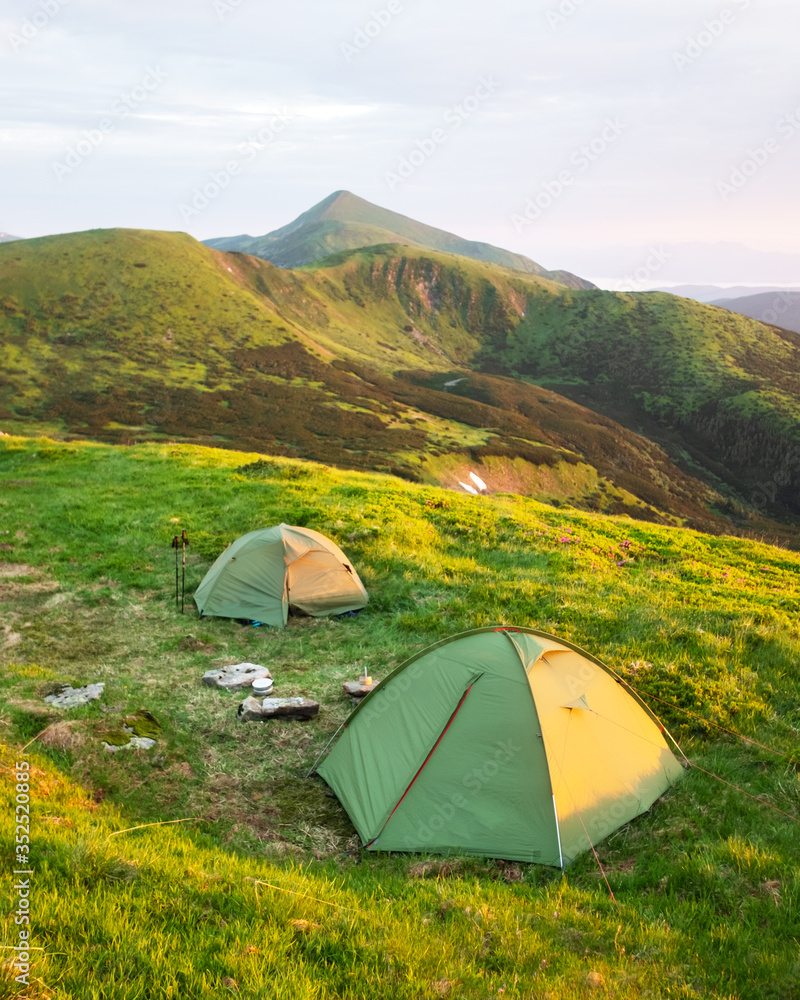 Two green tents on amazing meadow in spring mountains. Landscape photography, travel concept