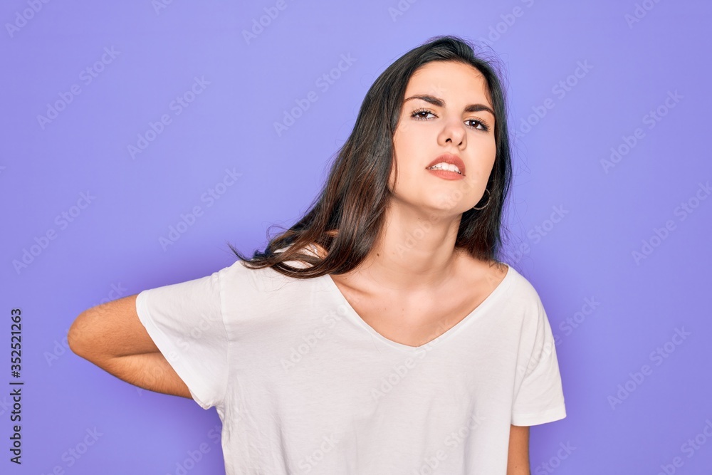 Young beautiful brunette woman wearing casual white t-shirt over purple background Suffering of backache, touching back with hand, muscular pain