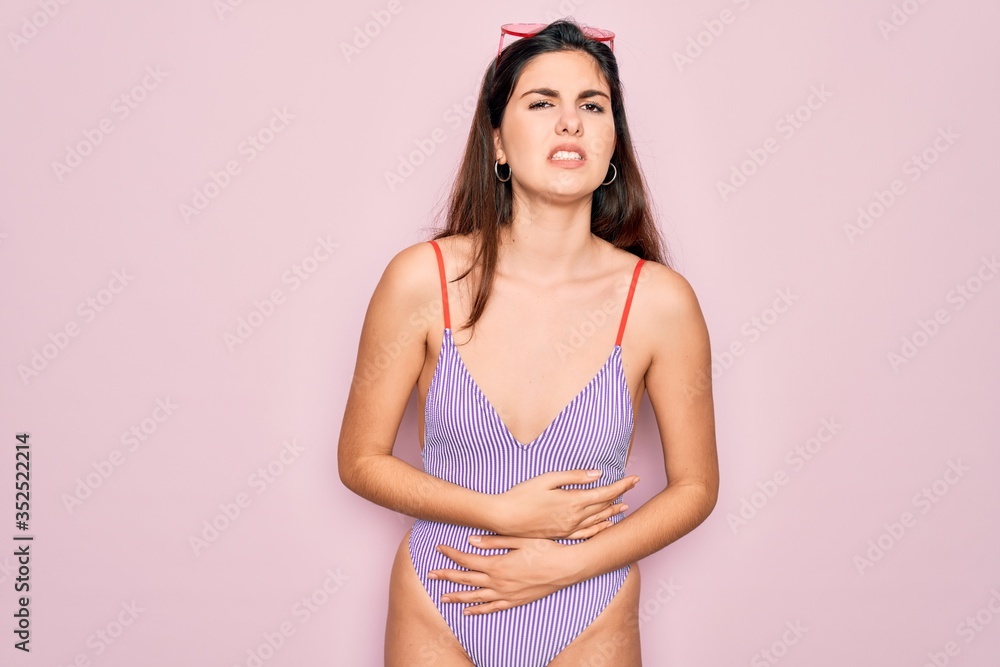 Φωτογραφία Young beautiful fashion girl wearing swimwear swimsuit and sunglasses over pink background with hand on stomach because indigestion, painful illness feeling unwell