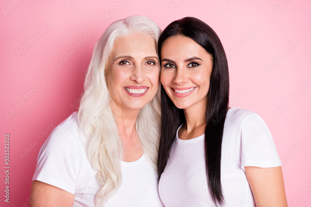 Photo of pretty old mother young daughter two ladies good mood stand close generation love comfort wear casual white t-shirts isolated pastel pink color background