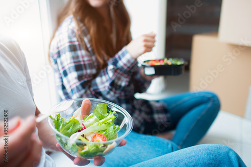 A young married couple in the living room in the house are sitting near the window and eat the first time in a new house. hey are happy about new home. Moving  buying a house  apartment concept.