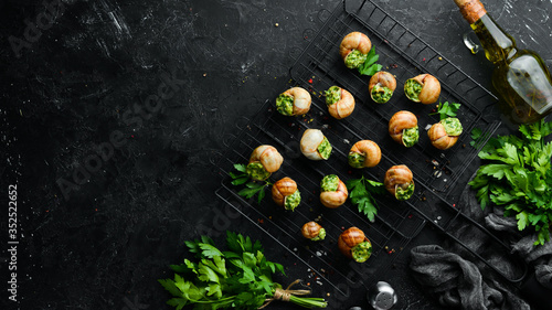French food. Baked snails with pesto sauce on a black stone background. Top view. Free space for your text.