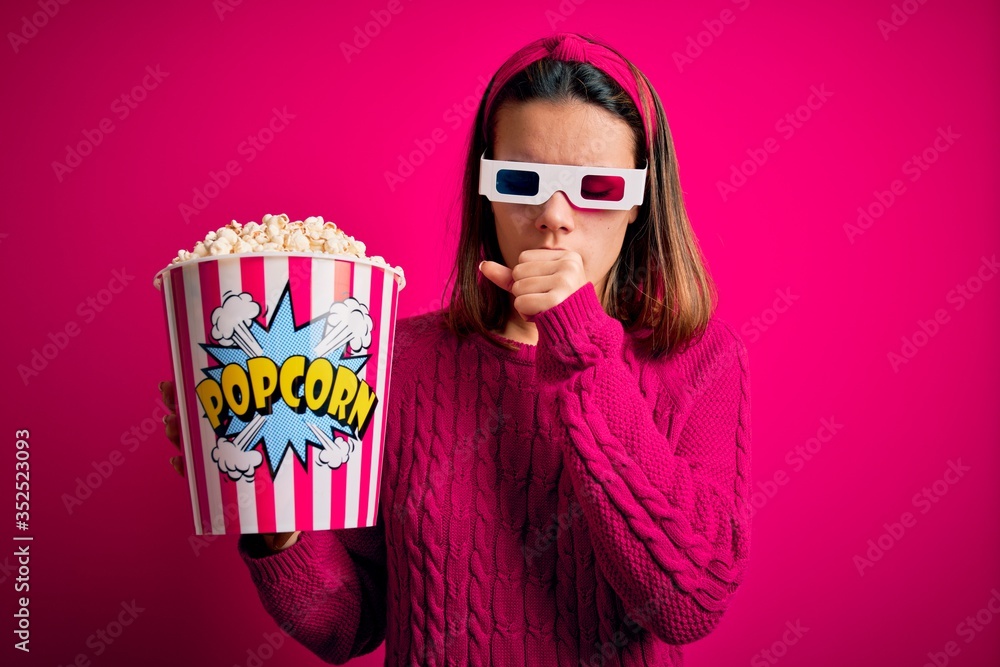 Obraz premium Young beautiful girl watching movie using 3d glasses eating box with popcorns feeling unwell and coughing as symptom for cold or bronchitis. Health care concept.