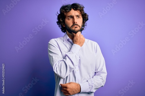 Fototapeta Naklejka Na Ścianę i Meble -  Young handsome business man with beard wearing shirt standing over purple background Thinking worried about a question, concerned and nervous with hand on chin