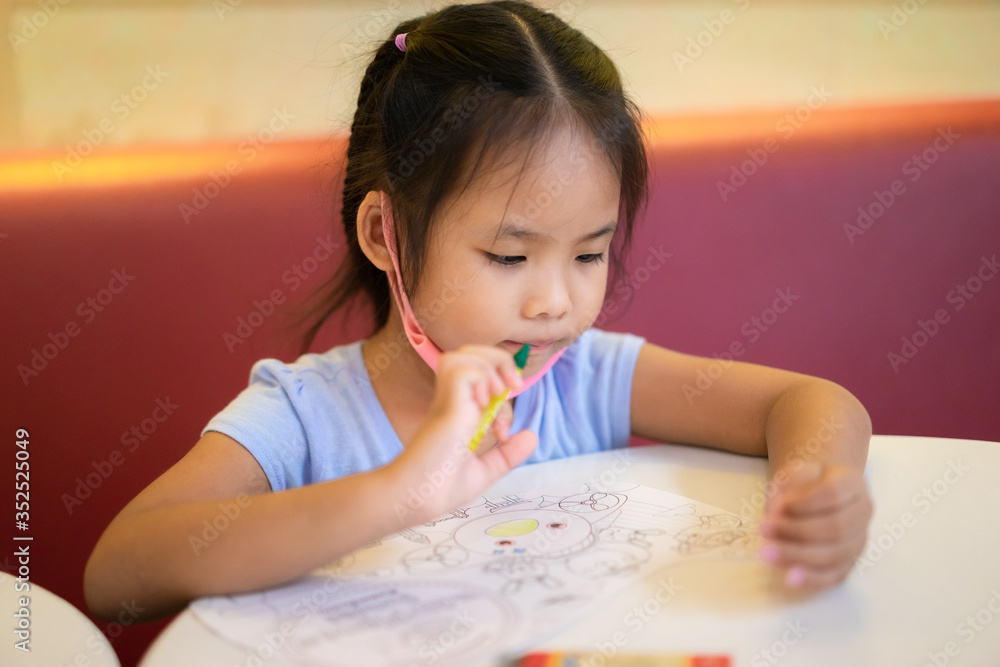 asian little girl sitting at table, drawing pictures with colored pencils in paper at home asian little girl sitting at table, drawing pictures with colored pencils in paper at home