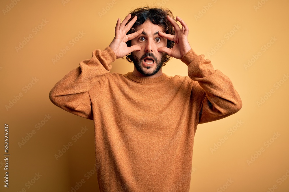 Young handsome man with beard wearing casual sweater standing over yellow background Trying to open eyes with fingers, sleepy and tired for morning fatigue Young handsome man with beard wearing casual sweater standing over yellow background Trying to open eyes with fingers, sleepy and tired for morning fatigue