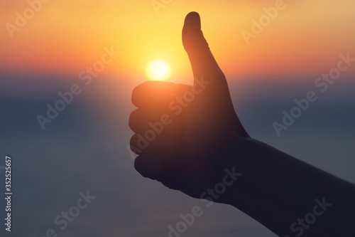 man shows thumbs up at sunset, agreement and solar power concept