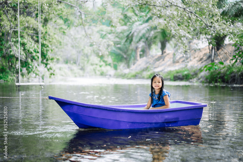 portrait of little asian girl sitting in blue boat in nature water