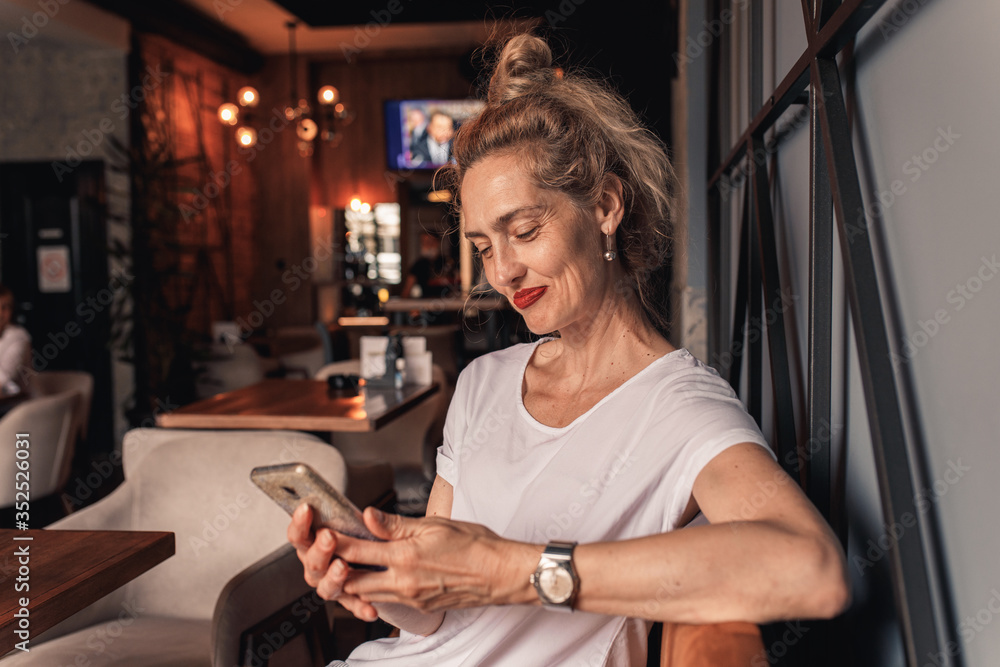 Smiling senior woman sitting in cafe drinking coffee and using smartphone. Smiling senior woman sitting in cafe drinking coffee and using smartphone.