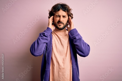 Young handsome sporty man with beard wearing casual sweatshirt over pink background covering ears with fingers with annoyed expression for the noise of loud music. Deaf concept.