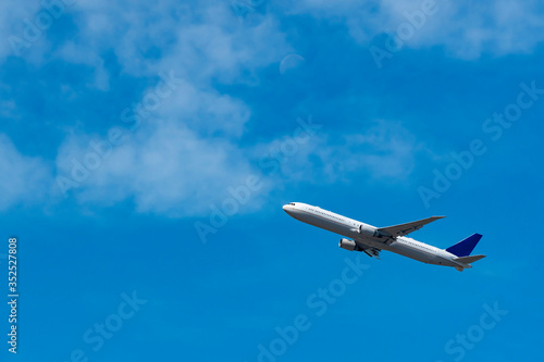 Airplane is flying on blue sky background with copy space. White soft clouds and a blurry half-moon visible